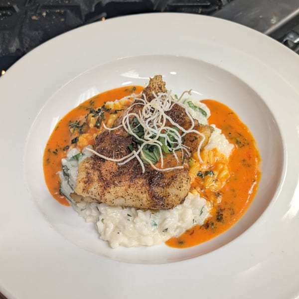 Pan-seared fish over risotto with a vibrant orange sauce, garnished with herbs and crispy strands.