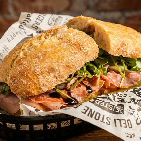 A ciabatta sandwich filled with prosciutto, arugula, and balsamic glaze, served in a basket.